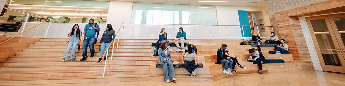 Students sitting on stairs talking. Another group of students walking down the stairs.